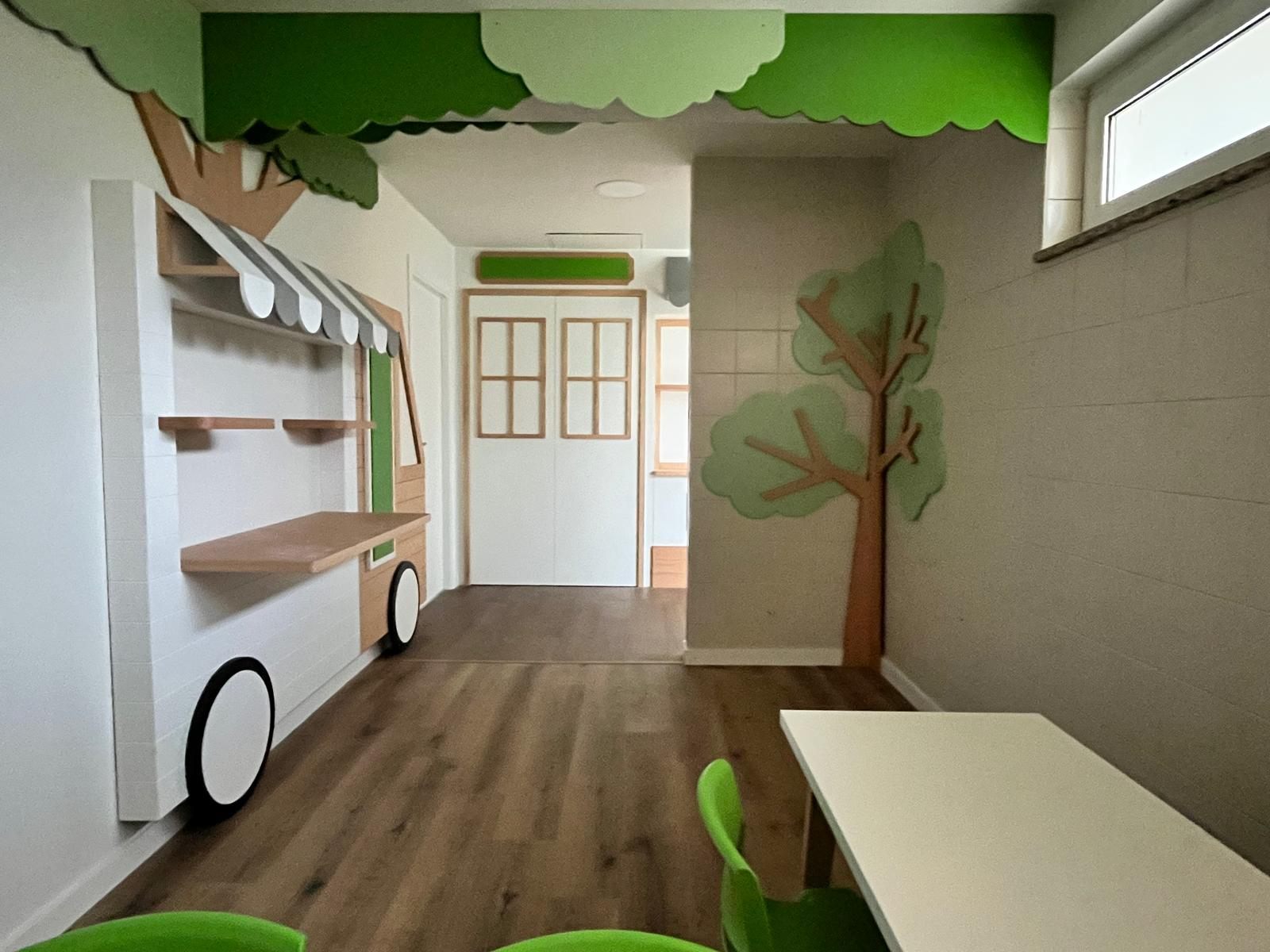 Carrito adosado a la pared con toldo y ruedas, junto a árboles recortados en madera