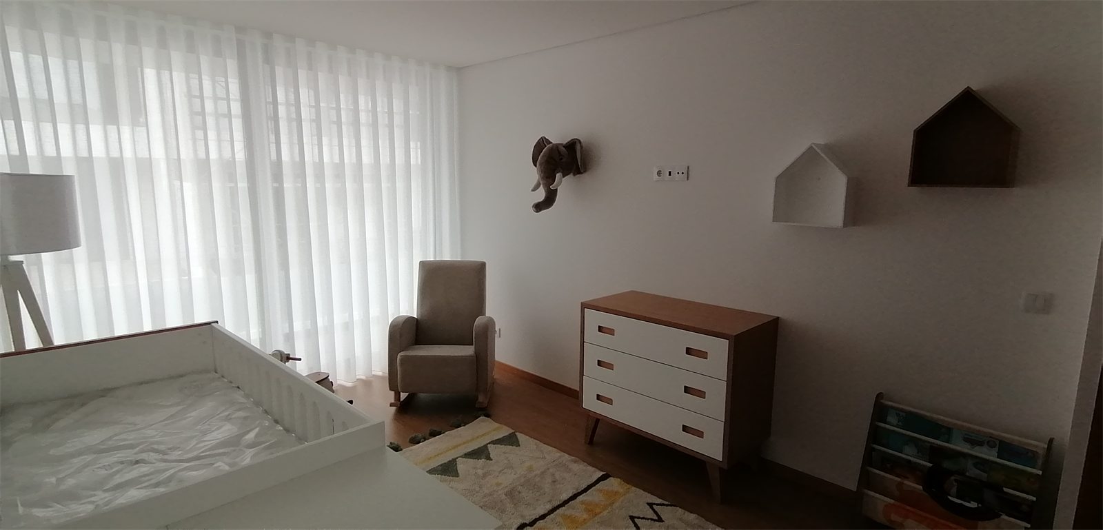 Cómoda de madera con butaca de lactancia junto a la ventana