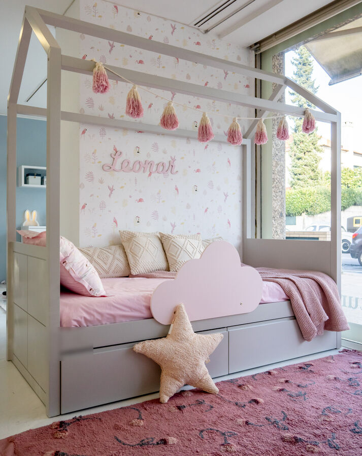 Cama casita infantil en tonos rosa con guirnalda de borlas